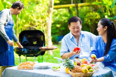 Park 'ta barbekü ızgara yemek partisi veren Asyalı mutlu bir arkadaş.