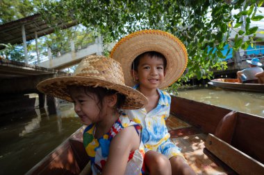 Mutlu çocuk ve kız Damnoen Saduak yüzen Tayland 'da seyahat nehri ahşap teknesinin keyfini çıkarıyorlar.