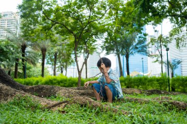 Asyalı anaokulu çocuğu şehir parkındaki yeşil tropikal ağaç ormanlarında geziyor.