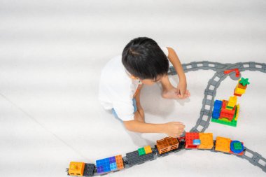 Mutlu anaokulu Asyalı çocuk beyazların eğitim odasında renkli oyuncak tren bloğu oynamaktan zevk alıyor.