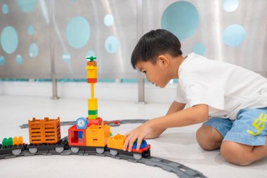 Mutlu anaokulu Asyalı çocuk beyazların eğitim odasında renkli oyuncak tren bloğu oynamaktan zevk alıyor.