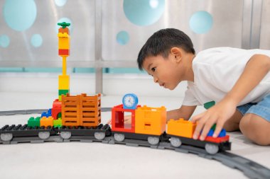 Mutlu anaokulu Asyalı çocuk beyazların eğitim odasında renkli oyuncak tren bloğu oynamaktan zevk alıyor.