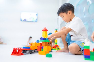 Mutlu anaokulu Asyalı çocuk beyazların eğitim odasında renkli oyuncak tren bloğu oynamaktan zevk alıyor.