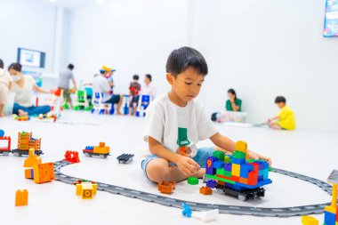 Mutlu anaokulu Asyalı çocuk beyazların eğitim odasında renkli oyuncak tren bloğu oynamaktan zevk alıyor.