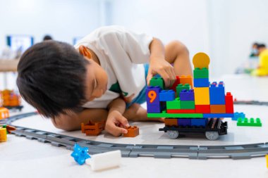 Mutlu anaokulu Asyalı çocuk beyazların eğitim odasında renkli oyuncak tren bloğu oynamaktan zevk alıyor.