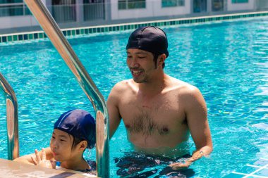 Güzel Asyalı kız babasıyla yüzme havuzunda yüzmekten zevk alıyor.