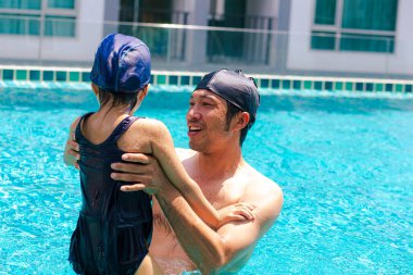 Güzel Asyalı kız babasıyla yüzme havuzunda yüzmekten zevk alıyor.