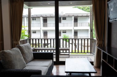 Otel odasındaki modern kanepe, perdeli ve halısı toprak tonunda, tropikal otel tesisinde dekore edilmiş.