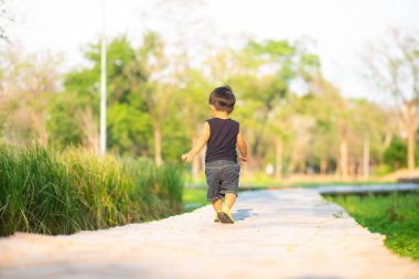 Yeni yürümeye başlayan Asyalı 1-2 yaşındaki çocuk ilk kez dışarıda yürüyor çayır çimenlerde gün batımında mutlu yeni bir hayat kavramı