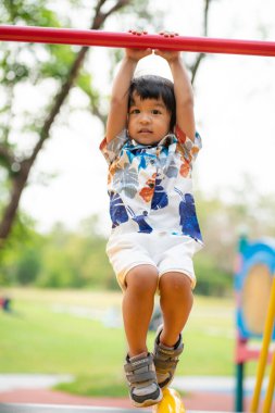 Sevimli anaokulu çocuğu şehir parkındaki çocuk spor salonunda bar kaldırırken eğleniyor.