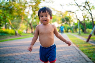 Küçük Asyalı çocuk şehir parkında gün batımında eğleniyor.