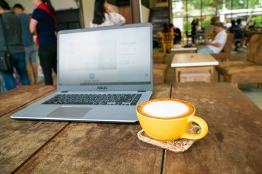 Ahşap masa üzerinde dizüstü bilgisayarlı sıcak latte sanat kahvesi çalışma alanı