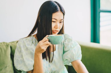 Yeşil kanepede oturan güzel Asyalı kadınlar sıcak latte kahve içerler.