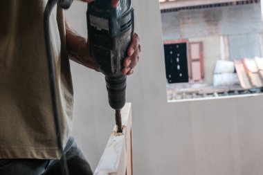 Yeni bina binasının ahşap kapısında elektrikli matkapla çalışan marangoz.