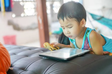 Küçük sevimli anaokulu çocuğu evde çizgi film izlerken tablet bilgisayar oynuyor.