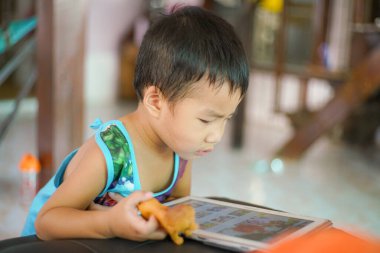 Küçük sevimli anaokulu çocuğu evde çizgi film izlerken tablet bilgisayar oynuyor.