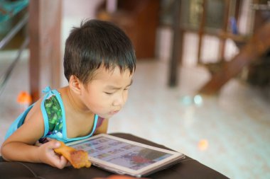 Küçük sevimli anaokulu çocuğu evde çizgi film izlerken tablet bilgisayar oynuyor.