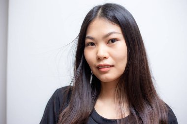 Güzel mutlu Asyalı kadın portresi beyaz arka planda siyah gömlek giyerek gülümsüyor.