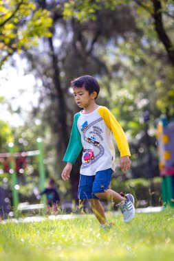 Anaokulu çocuğu çayırlarda koşuyor şehir bahçesinde oyun parkında mutlu çocuk.