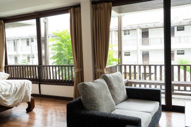Otel odasında, perde ve halı döşeli modern gri renkli kanepe. Toprak tonlu tropikal otel tesisinde dekore edilmiş.