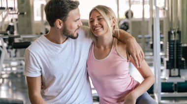 Spor adamı ve kadın spor salonunda oturup egzersizden sonra rahatlıyorlar.