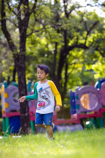 Anaokulu çocuğu çayırlarda koşuyor şehir bahçesinde oyun parkında mutlu çocuk.
