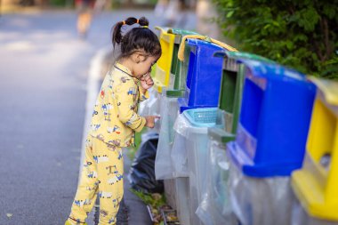 Sevimli küçük kız parkı temiz tutuyor. Çöpleri parktaki çöp kutusuna atıyor.