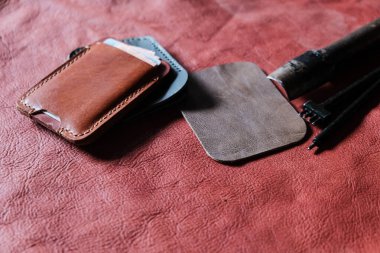 Hakiki kırmızı kahverengi deri kart yuvası deri arka planda el sanatları aracı ile çalışıyor