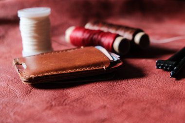 Hakiki kırmızı kahverengi deri kart yuvası deri arka planda el sanatları aracı ile çalışıyor