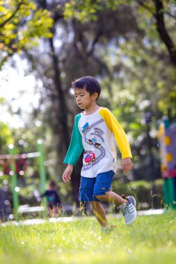Anaokulu çocuğu şehir parkında çimlerde koşuyor.