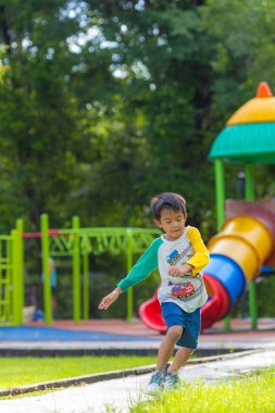 Anaokulu çocuğu şehir parkında çimlerde koşuyor.