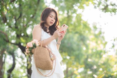 Güzel Asyalı kadın, doğada parktaki kadınlarda akıllı telefon eğlencesi kullanır.