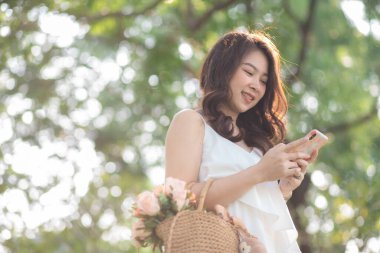 Güzel Asyalı kadın, doğada parktaki kadınlarda akıllı telefon eğlencesi kullanır.