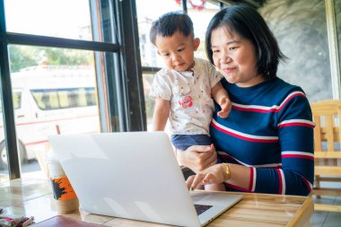 İşadamı Asyalı anne dizüstü bilgisayarda çalışıyor. Oğlu kahve dükkanında çalışıyor.