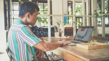 Asyalı baba internette bilgisayarla çalışıyor. Bebek bebekle kahve dükkanında oturuyor. 