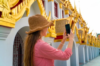 Güzel beyaz kadın Bangkok şehrinin tapınağında seyahat ederken fotoğraf çekmek için akıllı telefon kullanıyor.