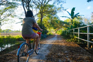 Küçük çocuk annesiyle birlikte gün batımında açık hava parkında bisiklet sürüyor.