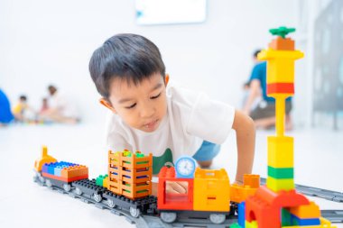 Küçük Asyalı anaokulu çocuğu beyaz oda eğitiminde oyuncak tren bloğunun tadını çıkarıyor ve öğreniyor, mantık kavramı geliştiriyor.