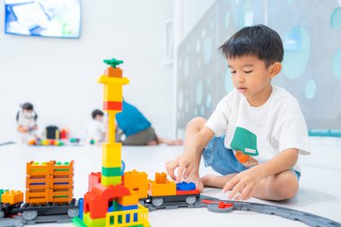 Küçük Asyalı anaokulu çocuğu beyaz oda eğitiminde oyuncak tren bloğunun tadını çıkarıyor ve öğreniyor, mantık kavramı geliştiriyor.