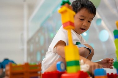 Küçük Asyalı anaokulu çocuğu beyaz oda eğitiminde oyuncak tren bloğunun tadını çıkarıyor ve öğreniyor, mantık kavramı geliştiriyor.