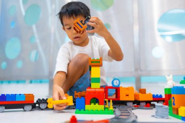 Küçük Asyalı anaokulu çocuğu beyaz oda eğitiminde oyuncak tren bloğunun tadını çıkarıyor ve öğreniyor, mantık kavramı geliştiriyor.