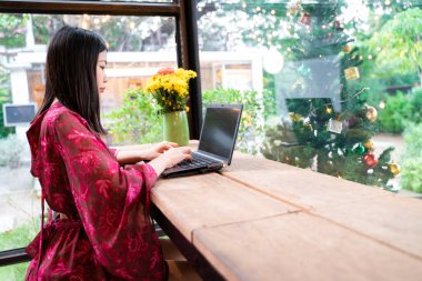Kırmızı elbiseli Asyalı iş kadını laptopunu kullanarak kafede oturuyor. İnternette konferans toplantısı var.