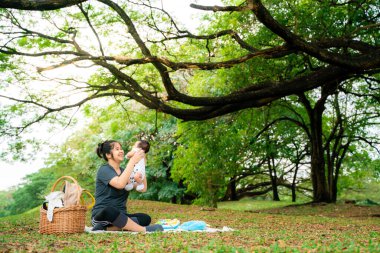 Asyalı anne, parkta piknikte bebekle oynuyor. Açık hava eğlencesi konsepti. 