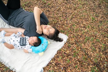 Asyalı anne, parkta piknikte bebekle oynuyor. Açık hava eğlencesi konsepti. 