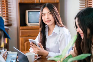 Gülümseyen Asyalı kadın takım çalışması internet üzerinden akıllı telefon ve dizüstü bilgisayarla merkez ofiste tartışıldı