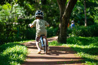 Şehir parkında bisiklet süren küçük mutlu çocuk, güneşli bir günde dışarıda egzersiz yapan.