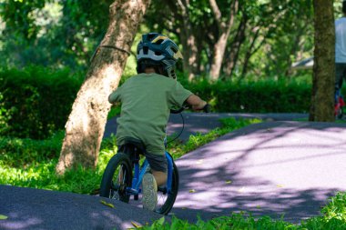 Şehir parkında bisiklet süren küçük mutlu çocuk, güneşli bir günde dışarıda egzersiz yapan.