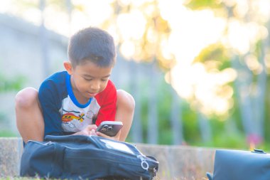 Küçük okul çocuğu açık hava parkında akıllı telefon oyunu oynuyor.