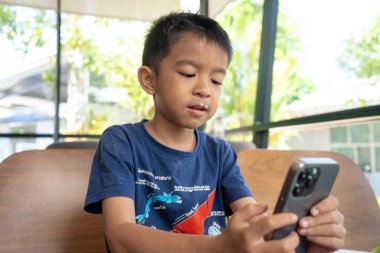 Küçük anaokulu çocuğu kafeteryada oturan akıllı telefonu kullanıyor.