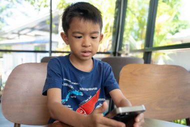 Küçük anaokulu çocuğu kafeteryada oturan akıllı telefonu kullanıyor.